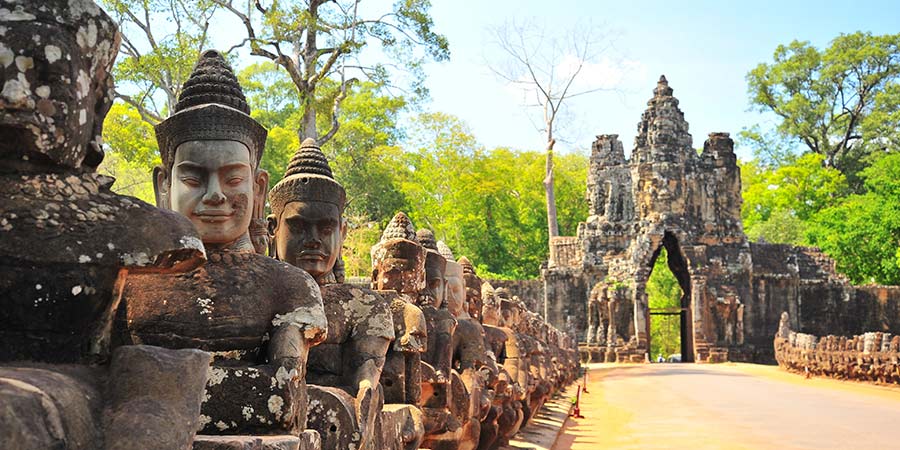 The stone gate of Angkor Thom, large stone statues line the path up to the gate. 